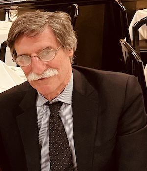 Man with brown hair, glasses and mustache in brown suit