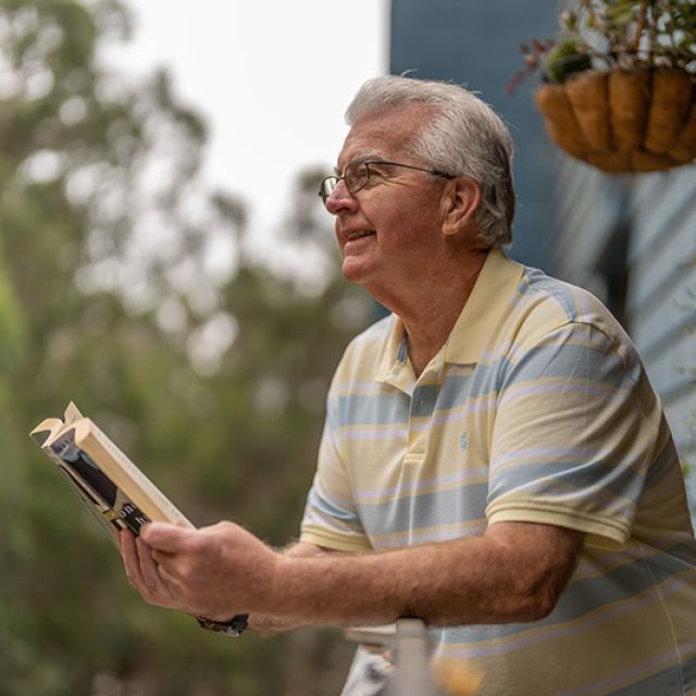 A man with gray hair reading a book outside 