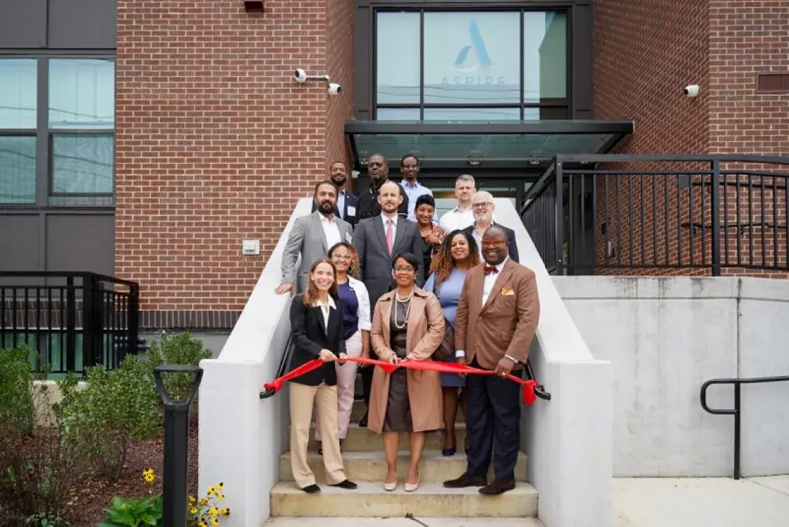 People in business attire standing on a stairway behind a red ribbon. 