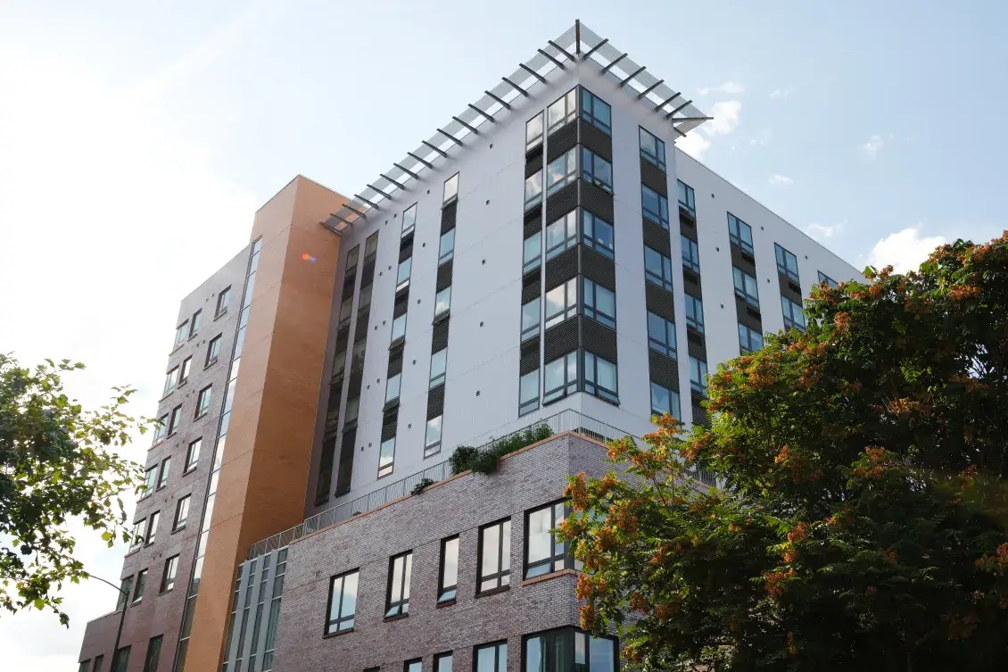 Modern high-rise apartment building flanked by trees and light blue sky 