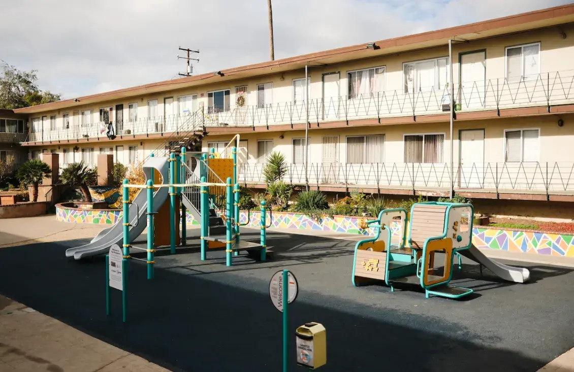 Picture of three-story cream apartment building with playground in foreground