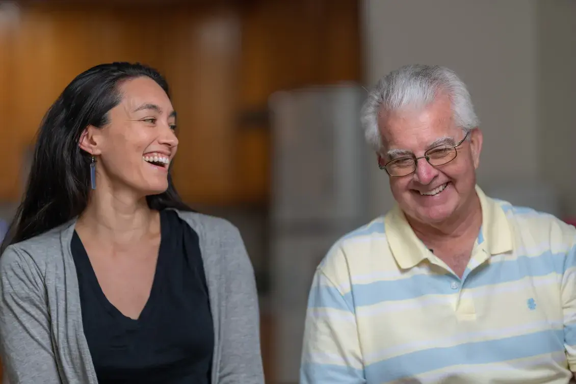 Two people sit side by side smiling and laughing.