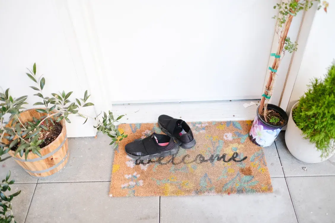 A welcome mat with shoes in front of a doorway with flower pots on both sides