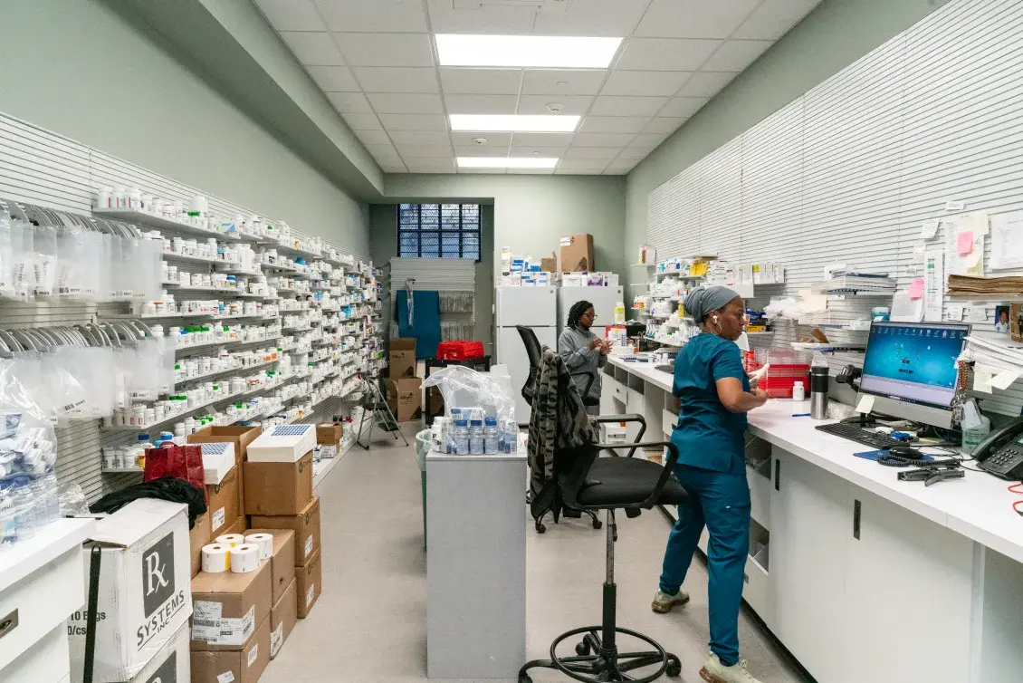 Two women working at computers in a fully stocked pharmacy.