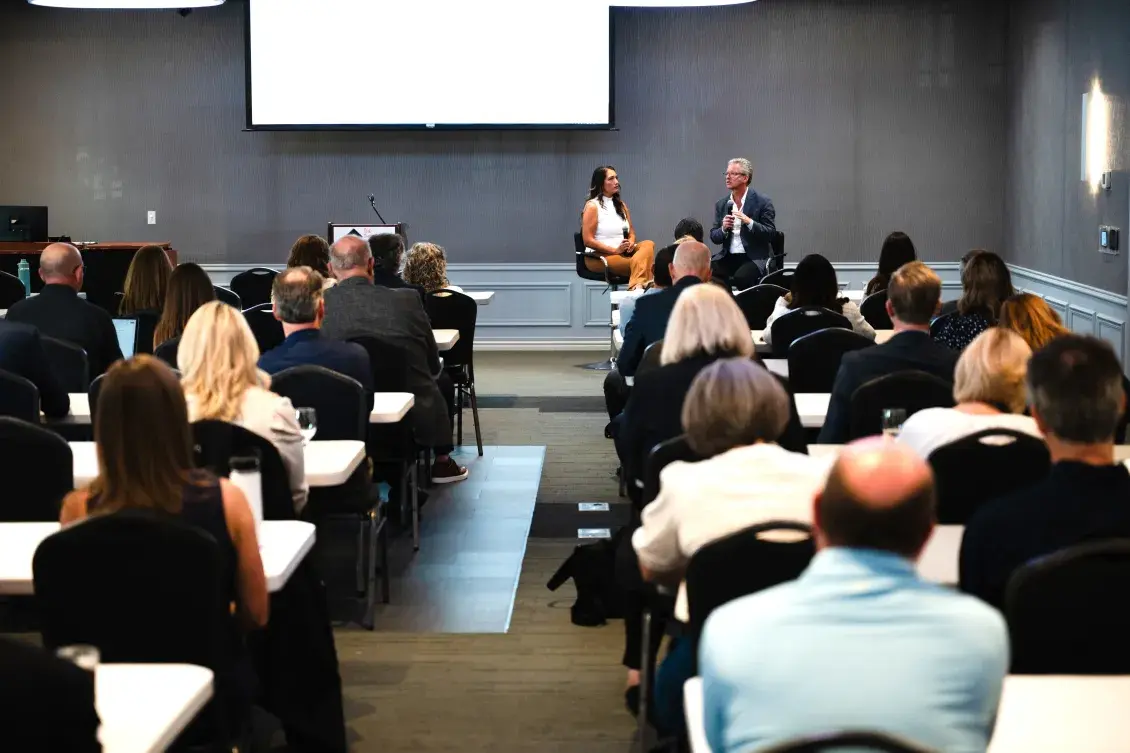 Two people seated at front of room talking with audience before them