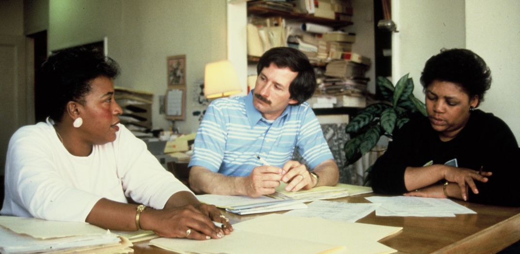 white male and two Black women sitting at a table in discussion