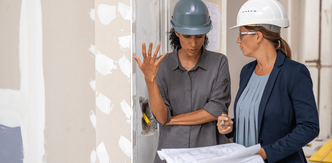 Two woman in construction hats talking on a job site