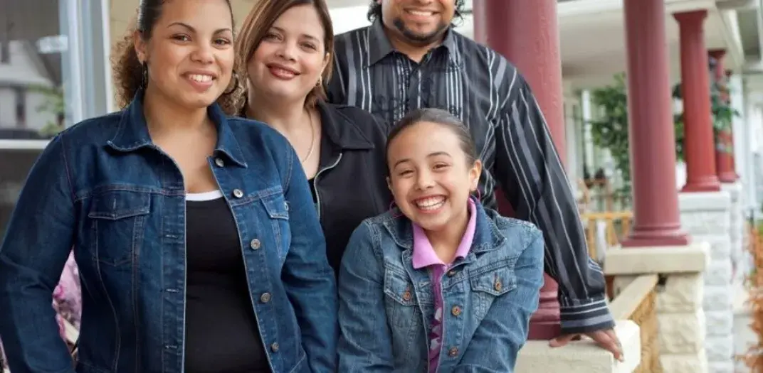 Family of four standing on a porch in front of a burgundy column