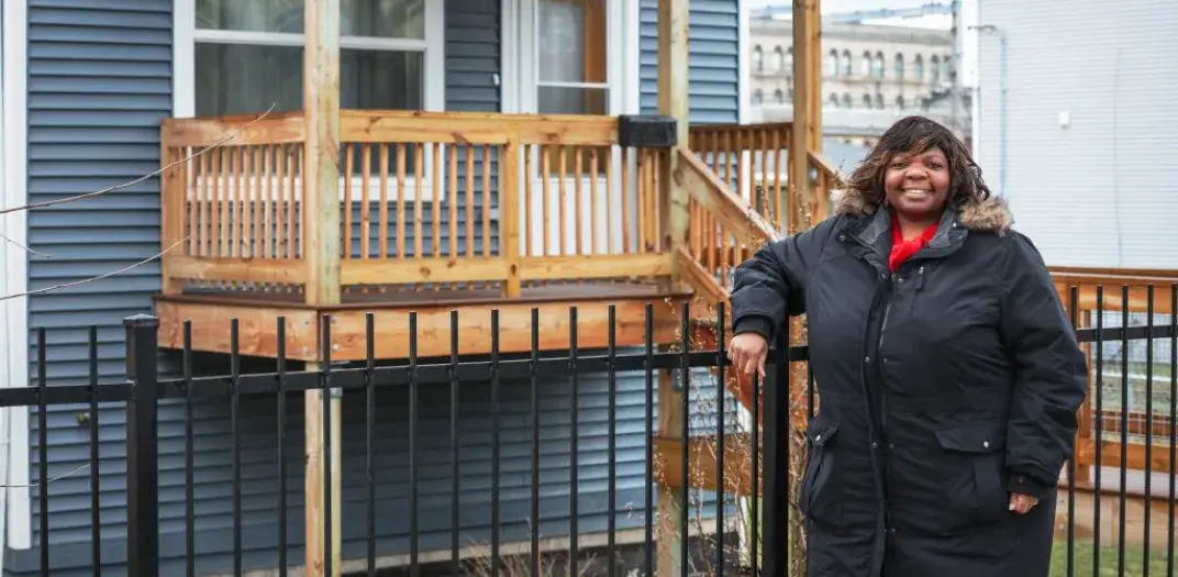 A person standing in front of a home leaning on a gate