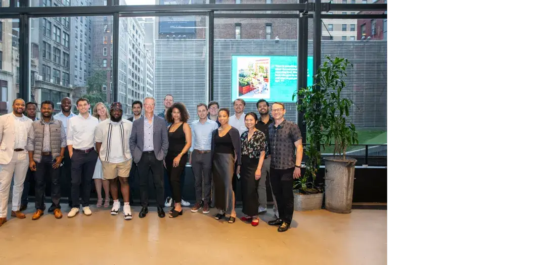 Gotham Society members stand with Shaun Donovan, Enterprise CEO, in front of tall windows with views of NYC skyscrapers