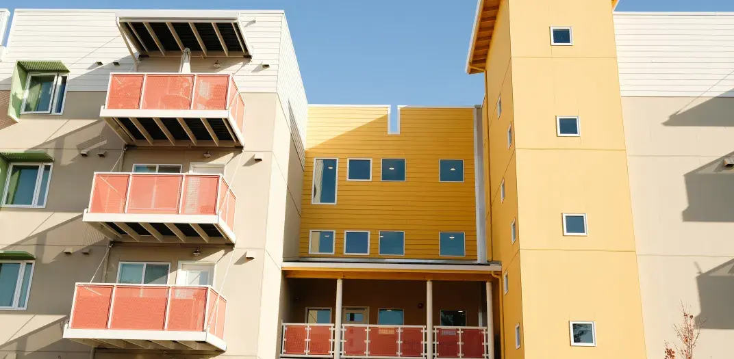 An apartment building with yellow painted columns and brick colored balconies