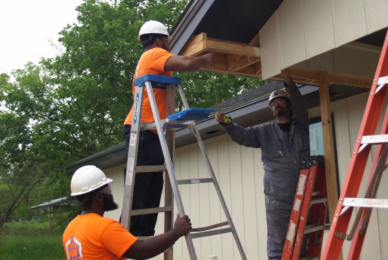 Men in orange clothing on ladders working on building
