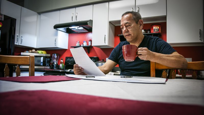 Man in dark shirt sitting at kitchen table drinking coffee and looking at paperwork