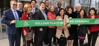 People standing behind a large green ribbon that says Gilliam Place Grand Opening