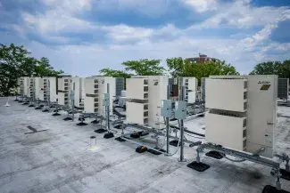 Row of rooftop heat pumps with trees, puffy white clouds, and blue sky in the background.