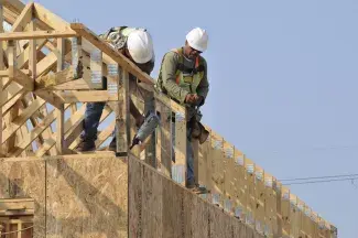 Two construction workers framing a roof on new housing