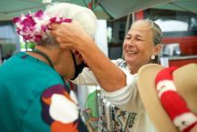 A Hawaiian woman greets a guest by putting a lei over her head.
