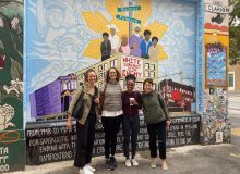 Photo of four women in front of colorful mural