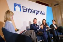 Panelists speaking on a stage with the word Enterprise on the wall behind them