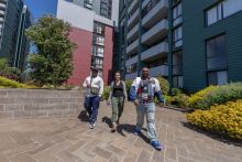 Three people walking forward with a tall apartment complex in the background. 