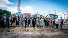 A line of people with green hard hats standing and holding matching green shovels at a groundbreaking ceremony