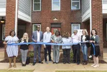 People cutting blue ribbon in front of new apartment building