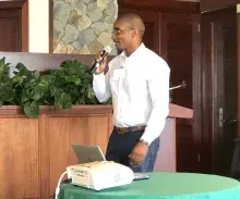 Jelani Newton holds a microphone beside a table with a projector on it