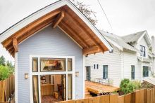 A newly built accessory dwelling unit (ADU) with light blue siding situated off the deck in the back of a larger single-family home. 