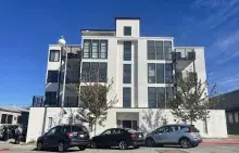 Four-story white apartment building with three cars parked out front