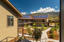 Courtyard of a multifamily housing development showing solar panels on the roof with a blue sky and white puffy clouds overhead and a mountain range in the background.