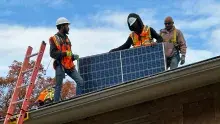 Three men installing a solar panel on a roof.
