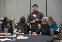 Man wearing glasses and dark, long-sleeved shirt speaking with women seated at table