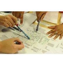 Five hands on a map. A finger points at the map; three hands are holding different colored pens.