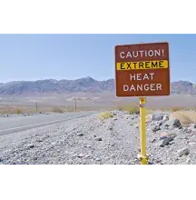Caution extreme heat danger sign on a dirt road with mountains in the back