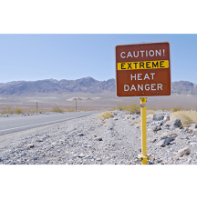 Caution extreme heat danger sign on a dirt road with mountains in the back