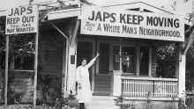 Woman stands in front of a house decorated with signs that uses a slur to Japanese with verbiage to keep moving and stay out  