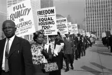 A line of people with signs marching for "full equality in house" and "freedom is equal housing"