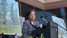 Woman stands at a podium with a microphone and an image of a housing development in the background