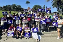 A group of people holding blue, Yes on Prop 5 signs in front of a park setting