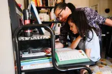 A mother helps her daughter with homework at a desk in an office