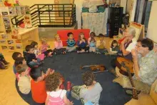 Children sitting on the floor in a circle participating in a music lesson
