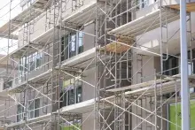 Scaffolding surrounds a multi-story residential building under construction, with partially installed windows and exterior finishes visible.