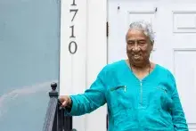 Emelda Paul stands on the steps of her front door with her hand on the railing