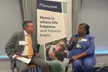 Woman in blue suit interviewing man in grey suit and striped, orange tie.