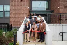 People in business attire standing on a stairway behind a red ribbon. 
