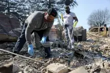 People wearing jeans, work shirts, and masks picking through debris after a wildfire