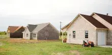 Three light colored brick homes with a riding lawn mower next to one