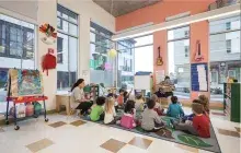 Children sit on the floor as they listen to an instructor in a colorful classroom