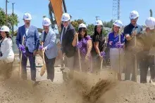 A group of people use shovels to dig into the ground at a groundbreaking ceremony