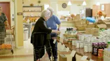 Two women looking at canned and jarred food on table.
